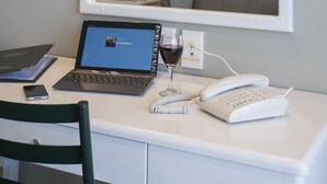 A hotel room with a desk, laptop, wine glass, phone, and a book.