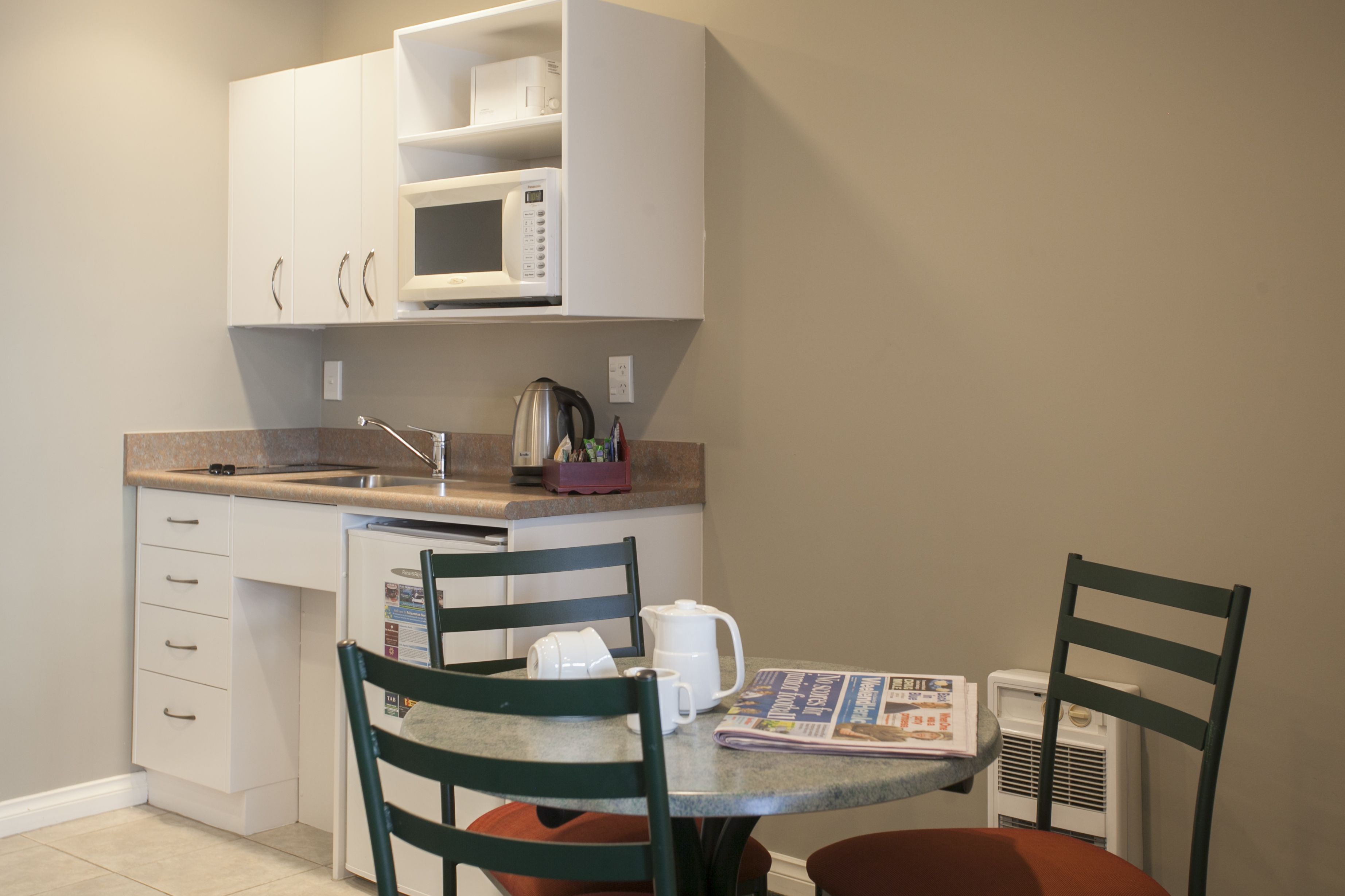 A compact kitchen with a microwave, sink, and a small dining area with chairs and a table.