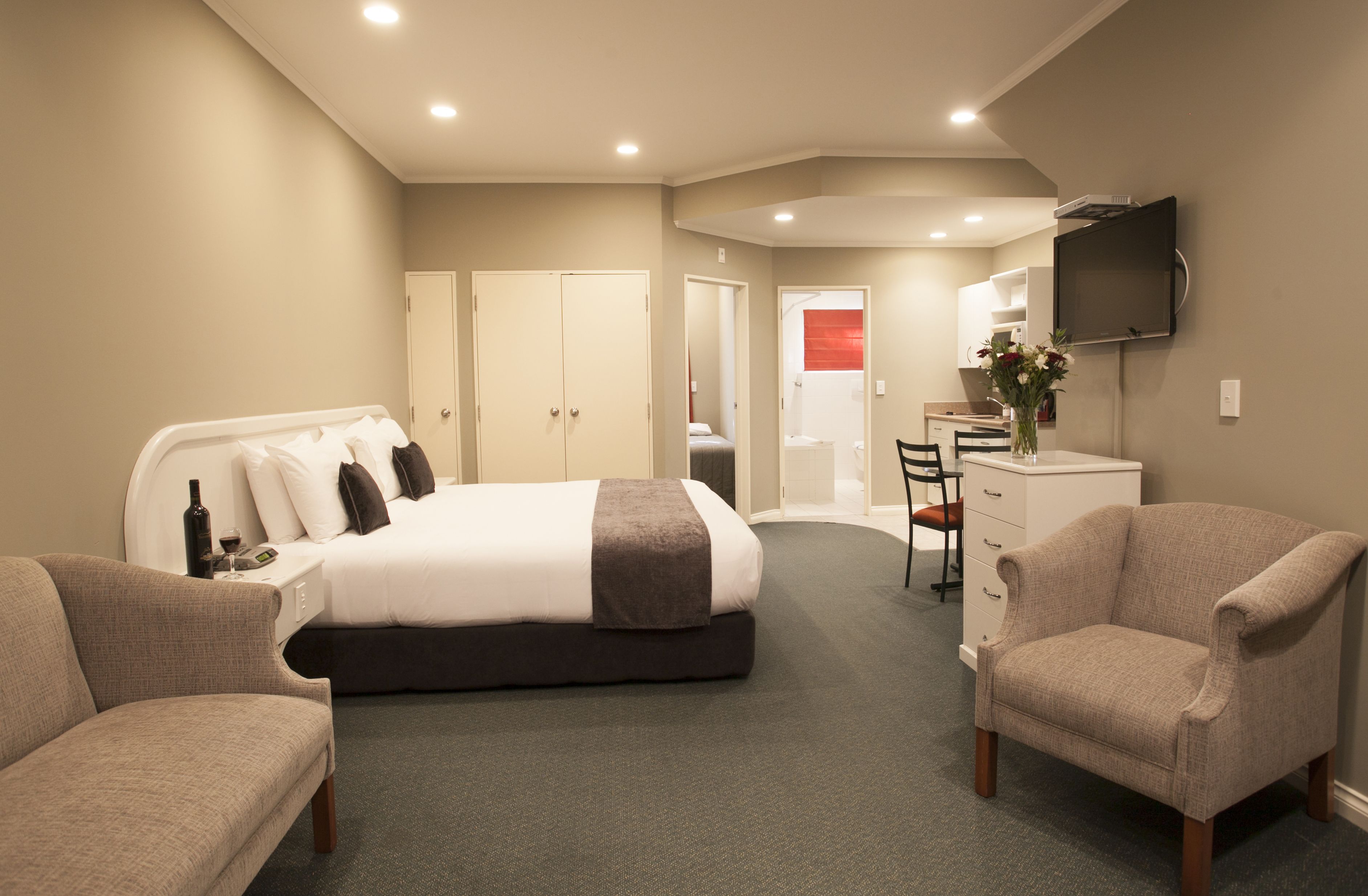 A hotel room with a bed, two armchairs, a desk, and a television.