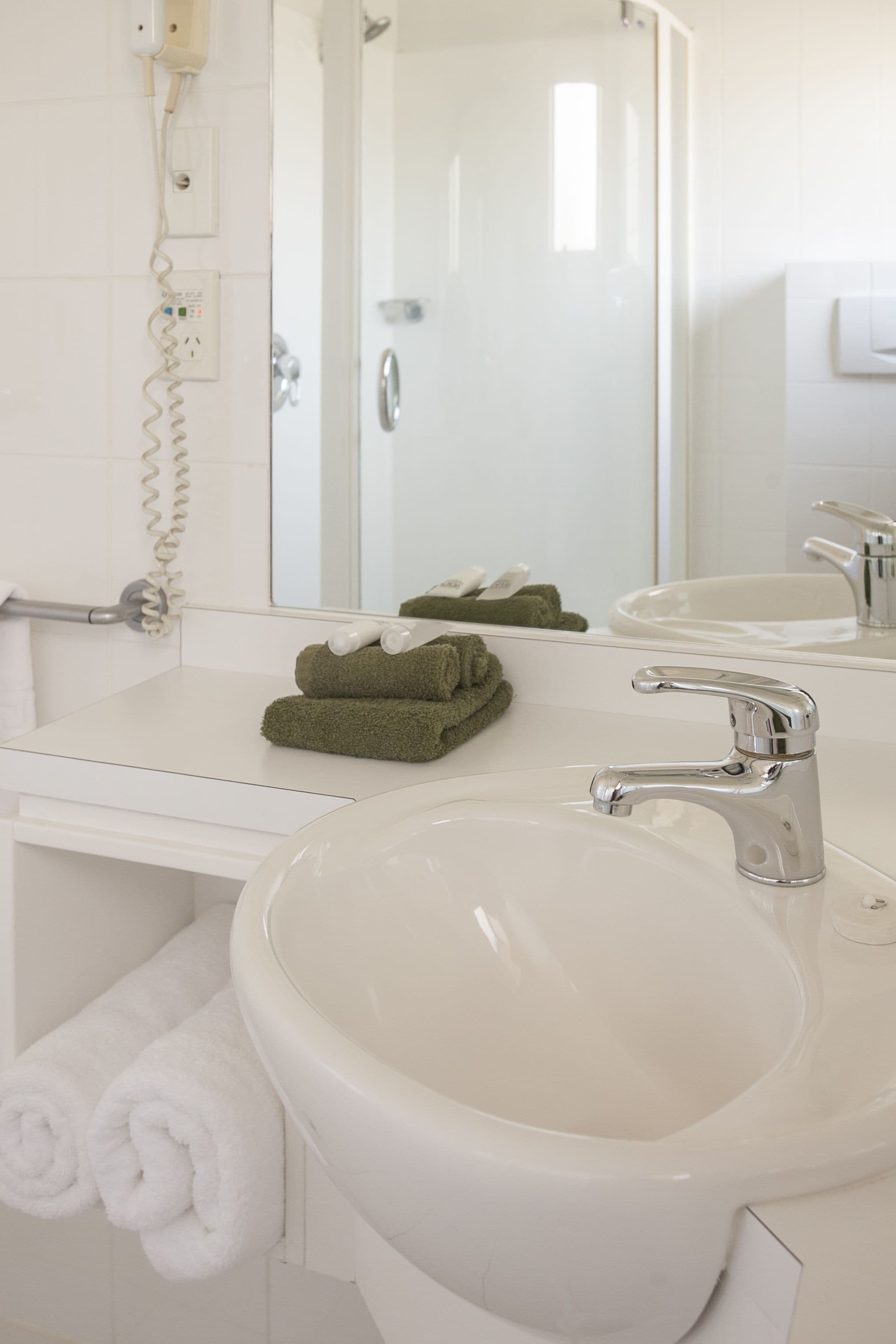A bathroom with a white sink, a mirror, and a towel rack with green towels.