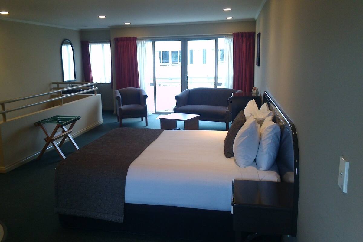 Ein Hotelzimmer mit einem großen Bett, zwei Sesseln, einem kleinen Tisch und einem Balkon mit Geländer.