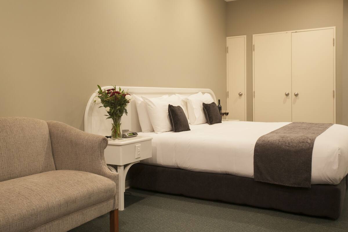 Ein Hotelzimmer mit Bett, Nachttisch, Blumenvase und einer Couch.