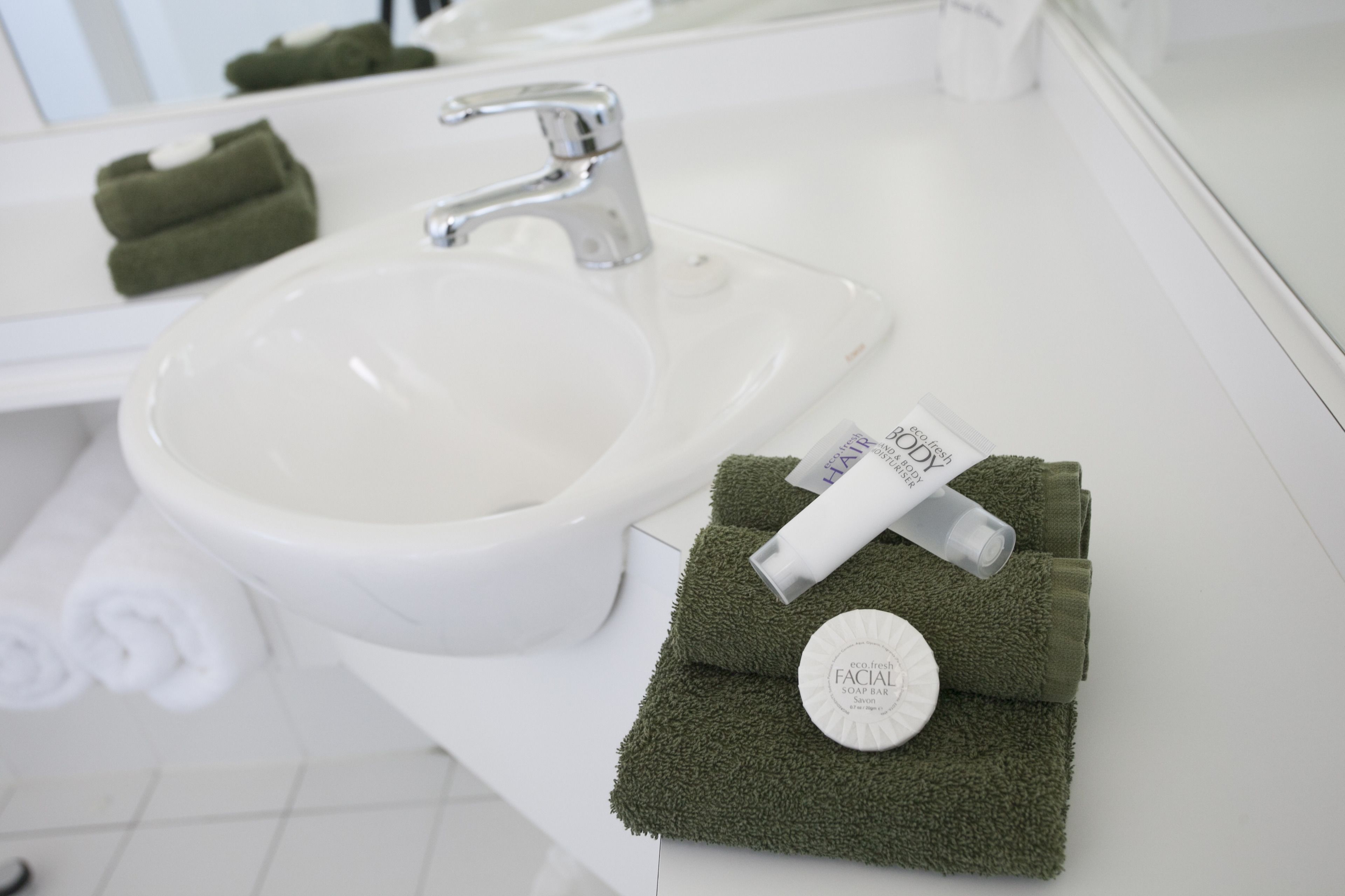A bathroom with a white sink, a mirror, and a green towel with a soap bar and a bottle on it.