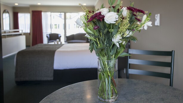 A hotel room with a bed, a table with a vase of flowers, and a chair.