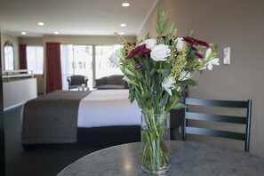 A hotel room with a bed, a table with a vase of flowers, and a chair. - Cornwall Motor Lodge (Palmerston North)