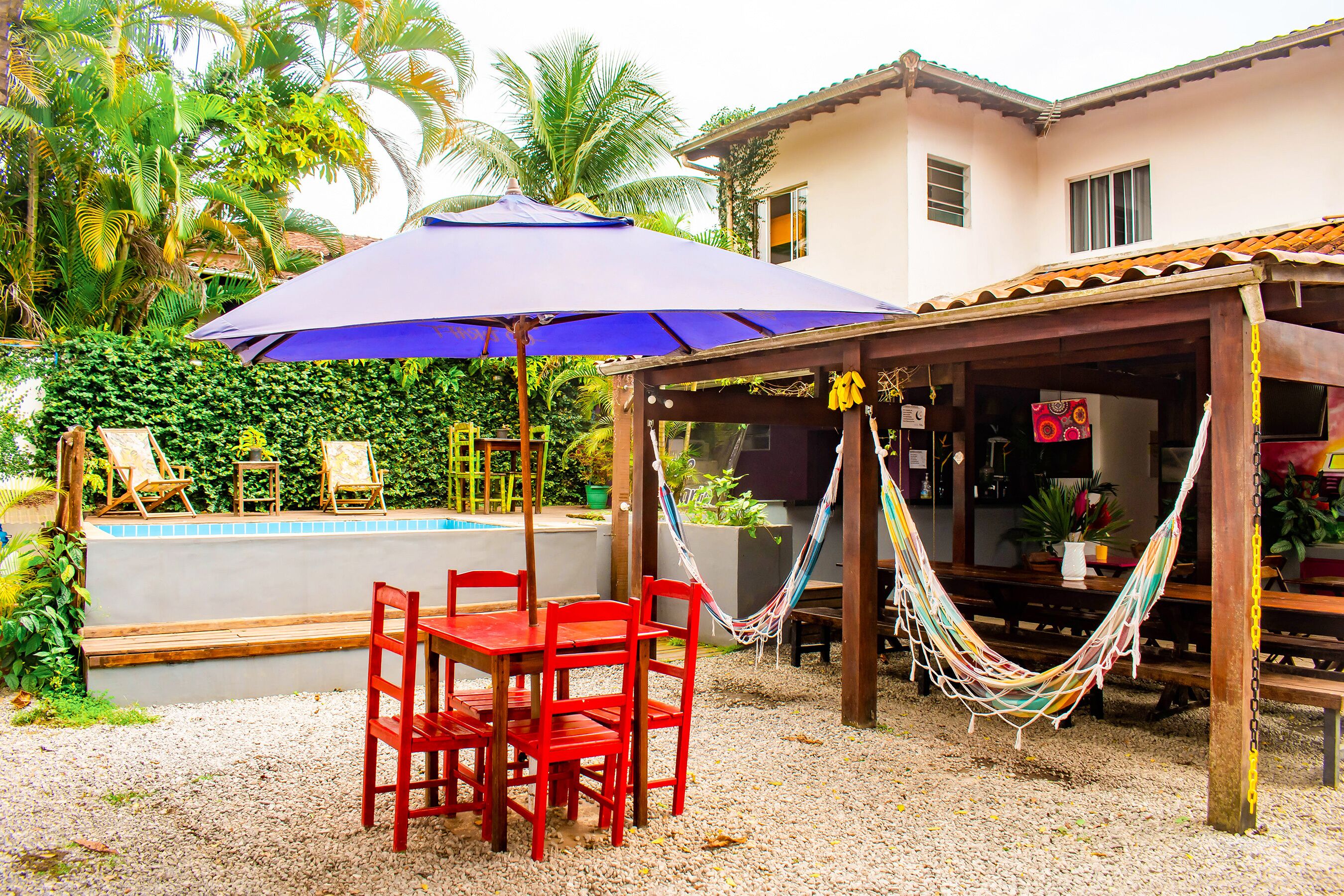 A pool area with a covered seating area, red chairs, and a hammock.