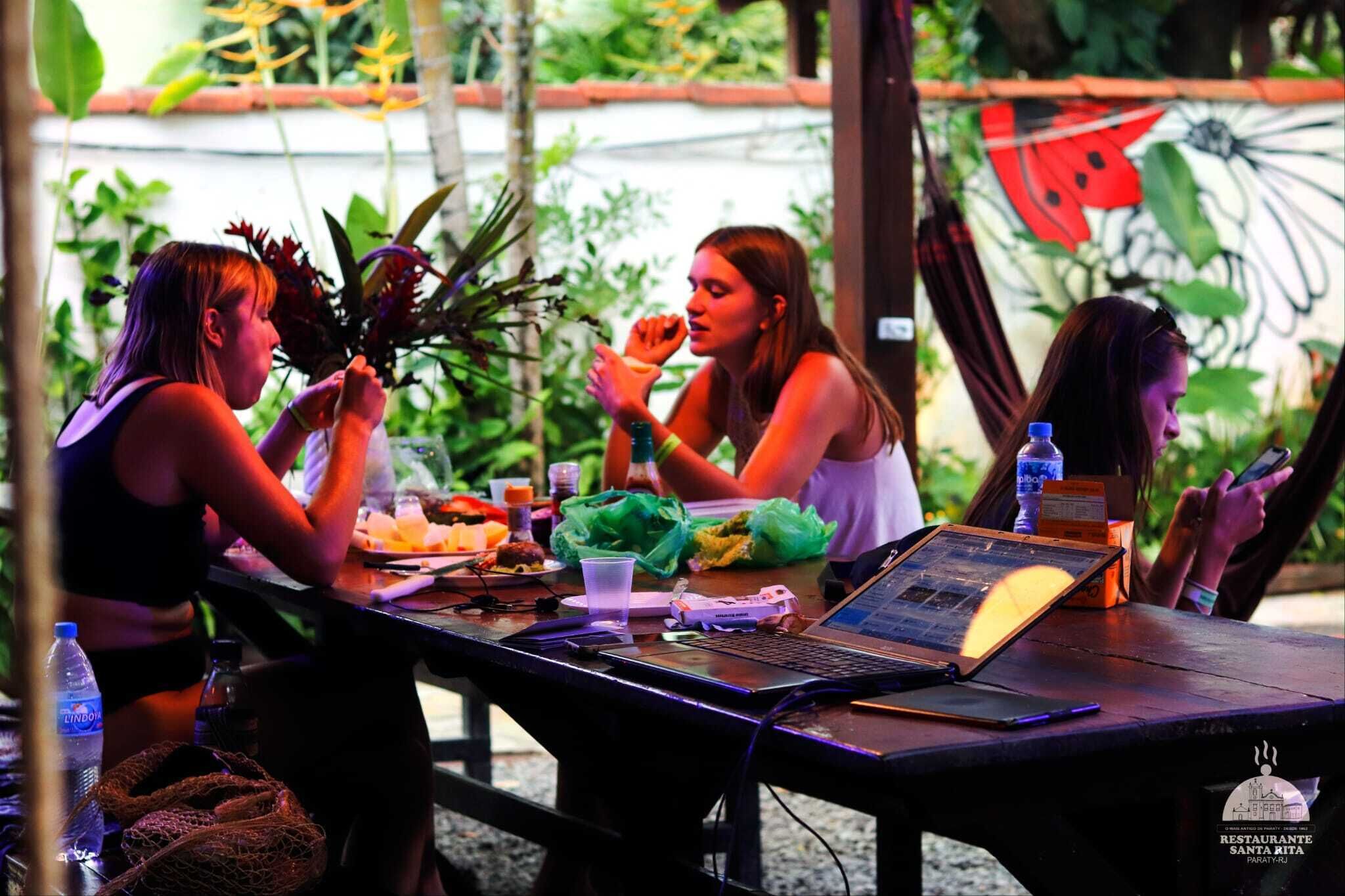 Un grupo de personas cenando en una mesa al aire libre, con una computadora portátil, botellas de agua y un menú.