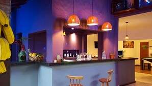 A bar area with two wooden stools, a counter with a mirror, and hanging orange pendant lights. - Che Lagarto Paraty - Hostel (Paraty)