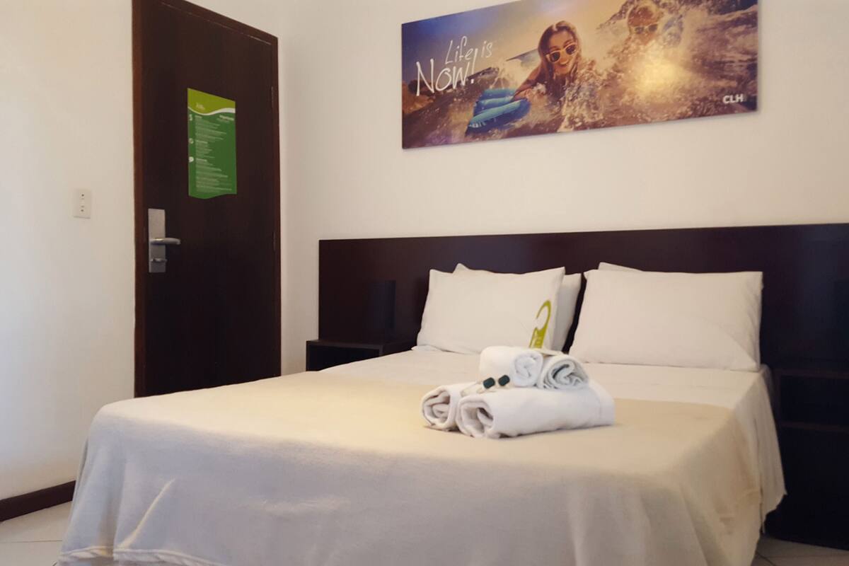 A hotel room with a neatly made bed, a wall-mounted sign, and a motivational poster.