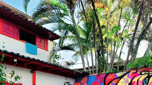 A pool area with a colorful mural, a red door, and a white building with red trim. - Che Lagarto Paraty - Hostel (Paraty)