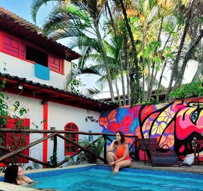 A pool area with a colorful mural, a red door, and a white building with red trim. - Che Lagarto Paraty - Hostel (Paraty)