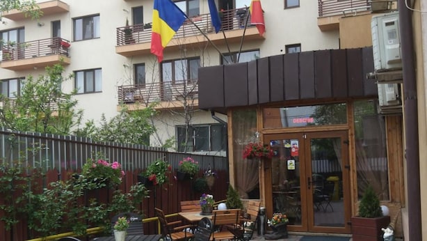 A courtyard with outdoor seating, a building with balconies, and flags. - La Casa (Bucharest)
