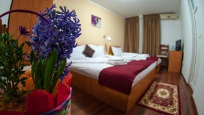 A hotel room with a bed, a desk, a chair, a window with curtains, and a decorative plant with purple flowers. - La Casa (Bucharest)