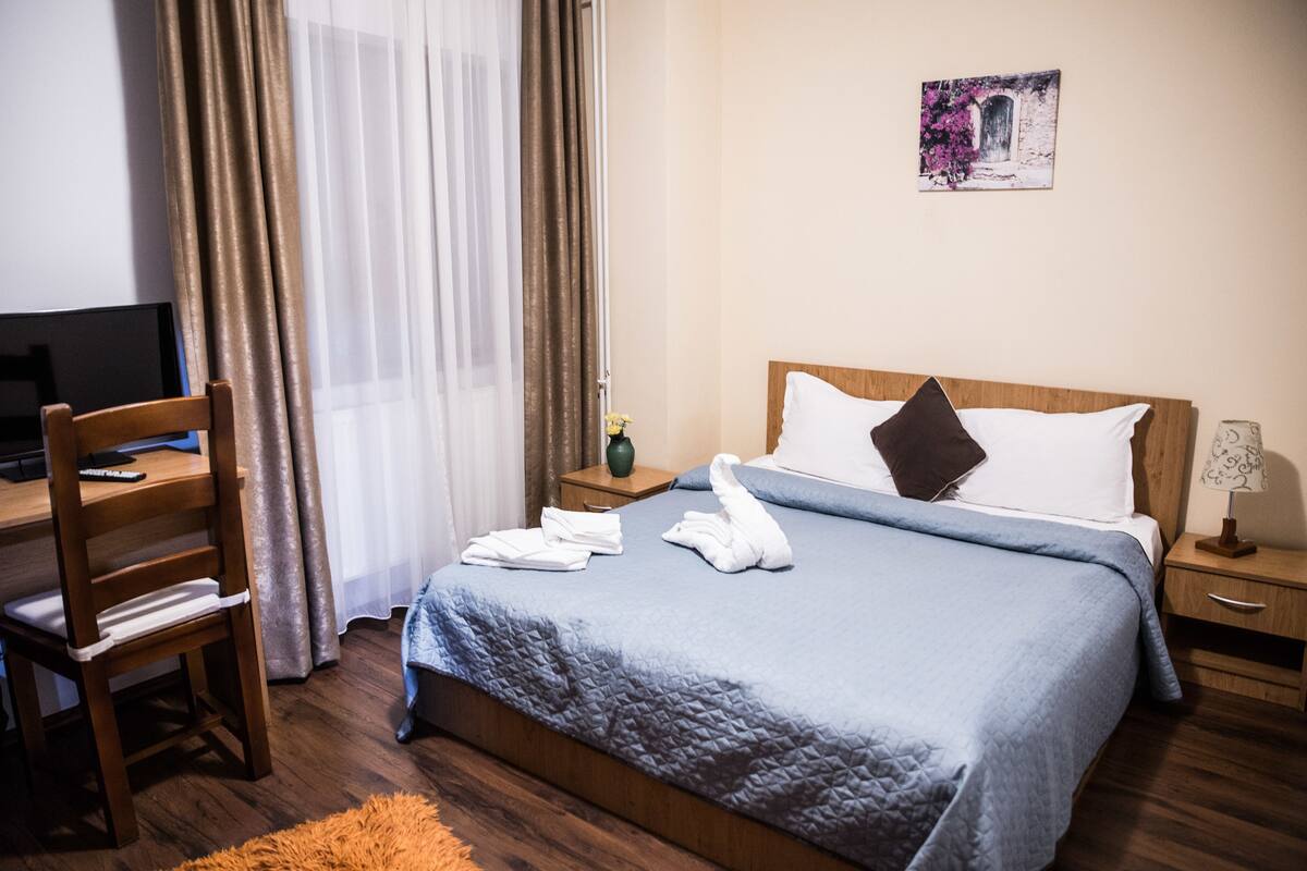 Una cama bien hecha con un edredón azul, un cabecero de madera y una mesita de noche con una lámpara.