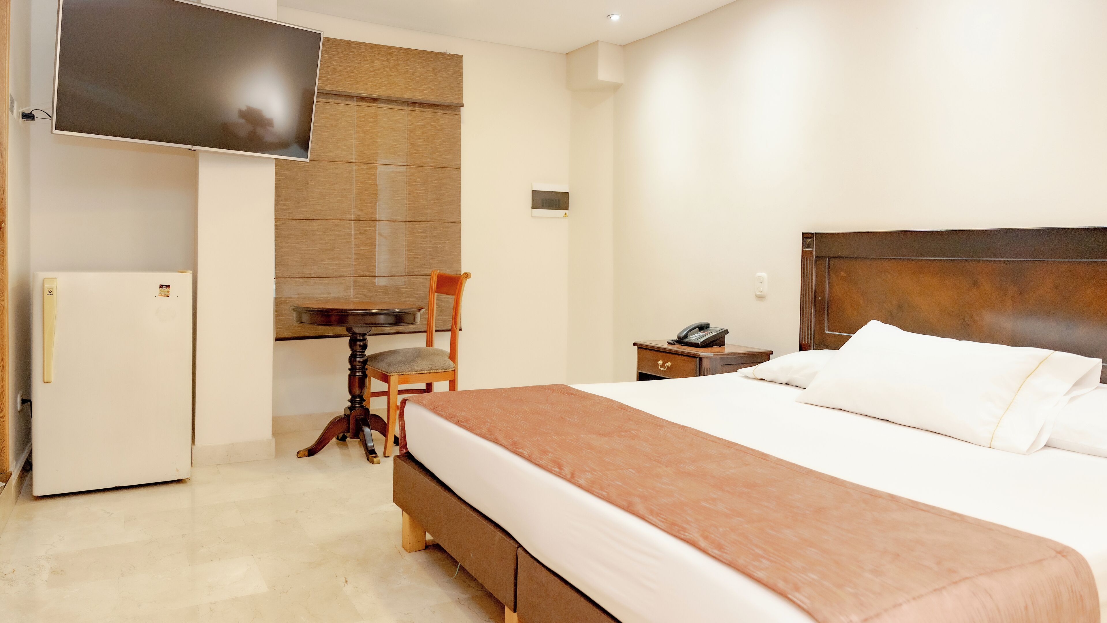 Quarto de hotel com cama, escrivaninha, cadeira, telefone e televisão.