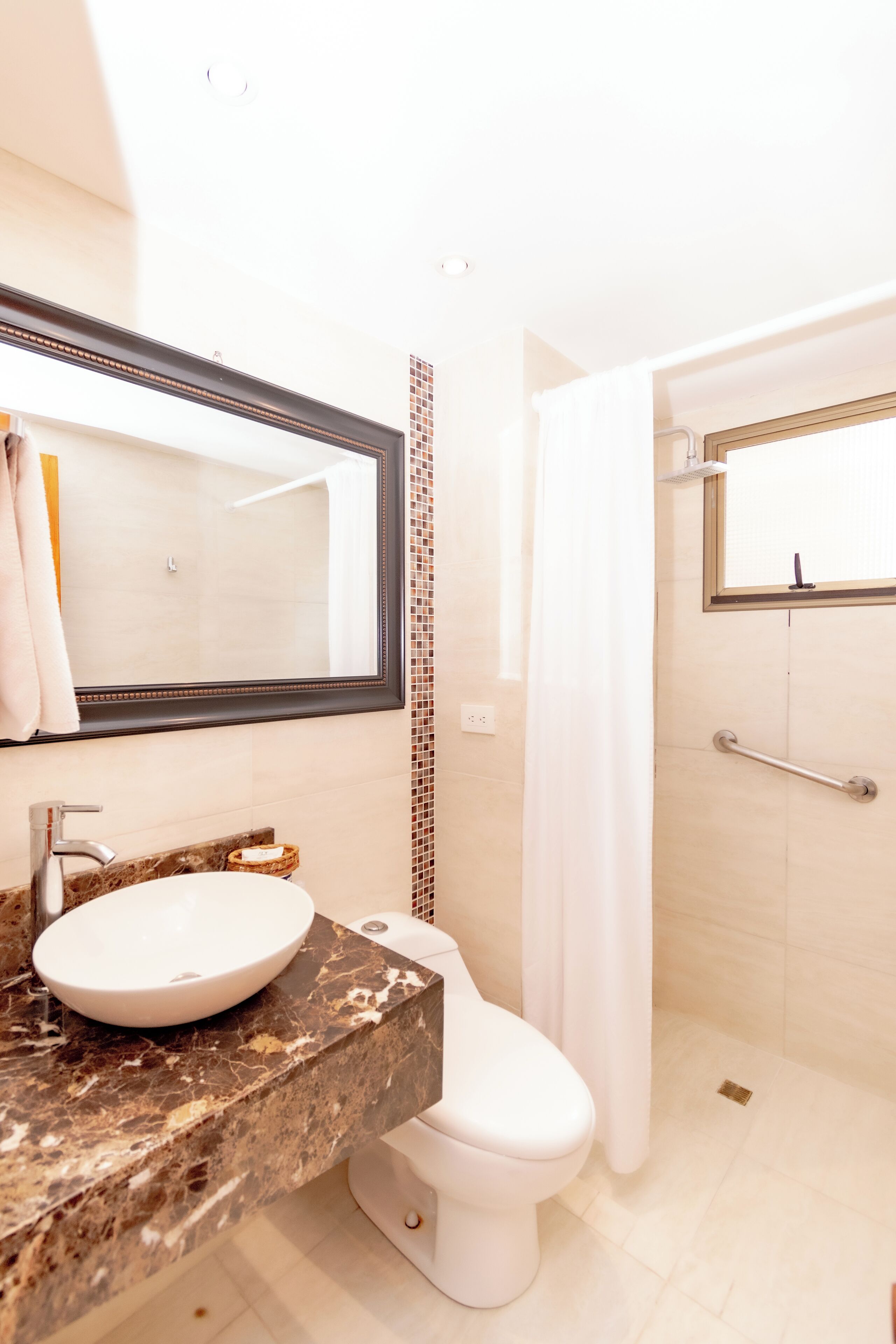 Een badkamer met een marmeren wastafel, een wit toilet, een douche met een handgreep en een spiegel met een decoratieve lijst.