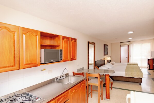 Una cocina compacta con armarios de madera, un microondas y una estufa a gas. Cuenta con una zona de comedor con una mesa y sillas.