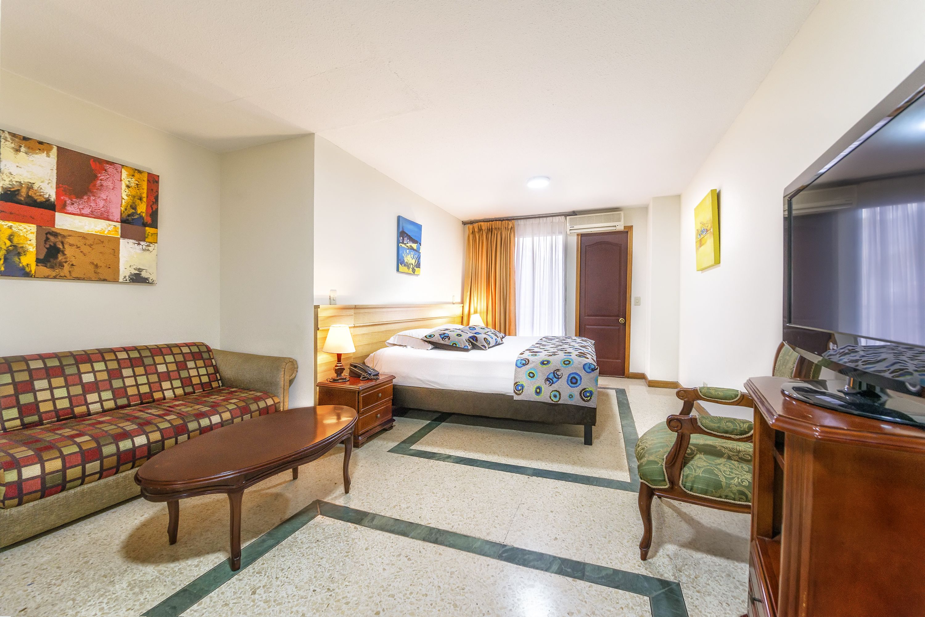 A hotel room with a bed, sofa, TV, and a painting on the wall.