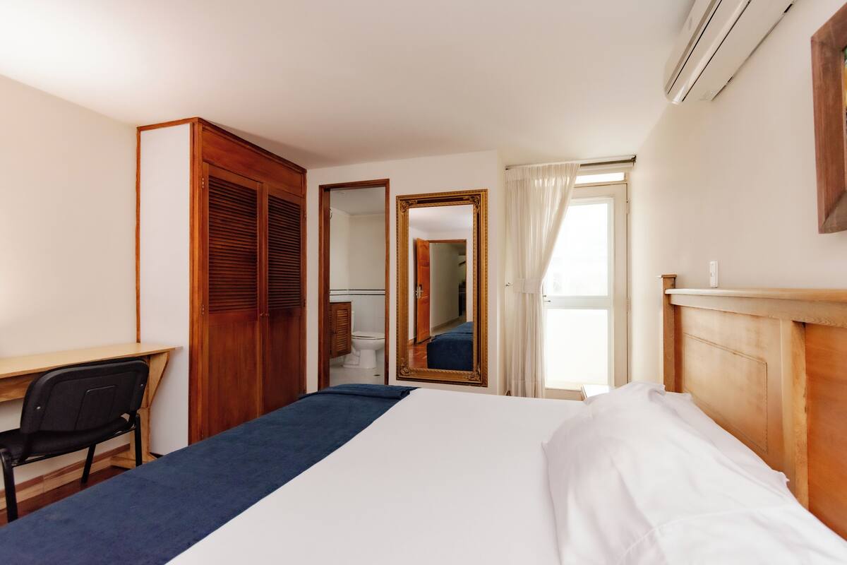A hotel room with a bed, a desk, a chair, a wardrobe, and a mirror.
