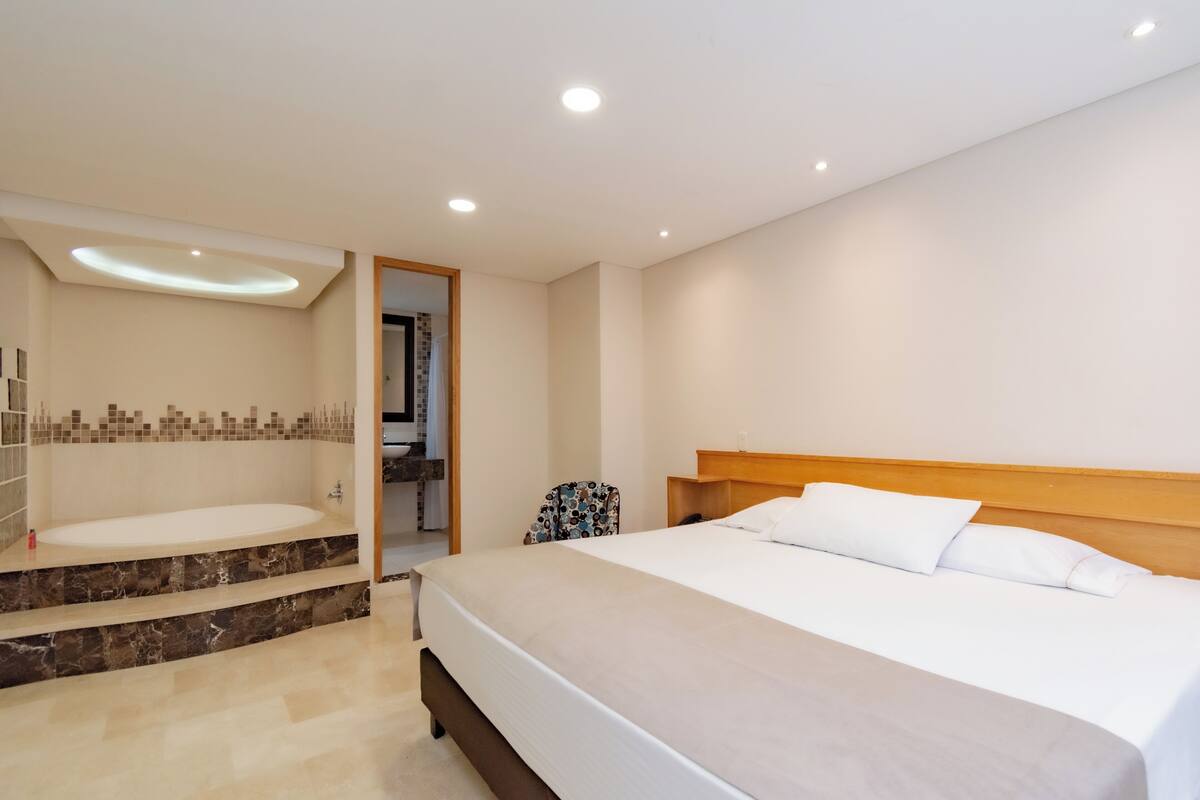 A modern hotel room with a large bed, a built-in bathtub, and a wooden headboard.