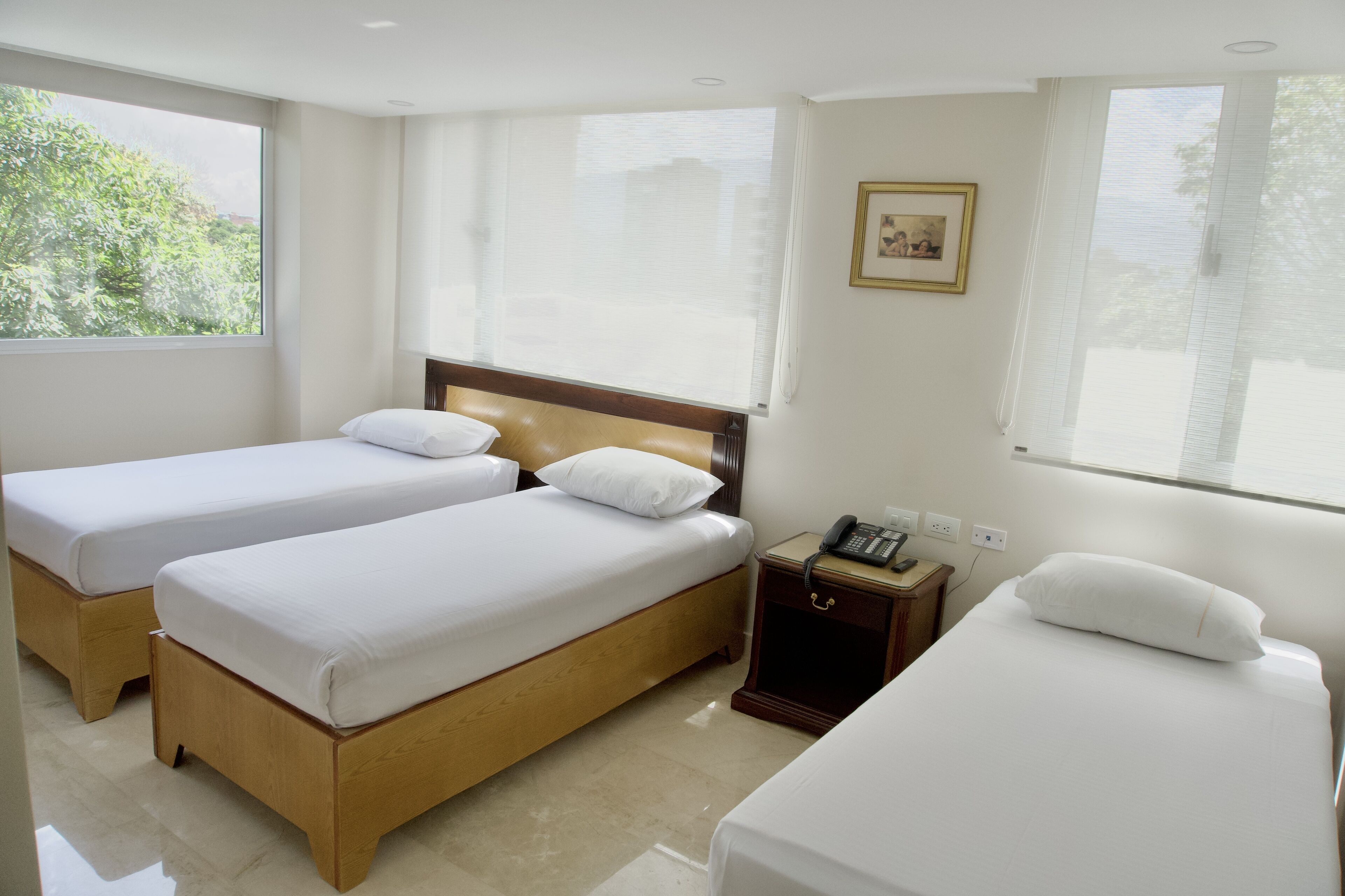 A hotel room with two single beds, a wooden headboard, a bedside table with a phone, and a window with blinds.