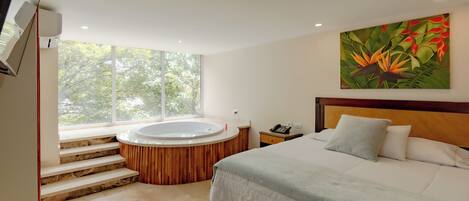 Un dormitorio moderno con una cama grande, cabecera de madera, un cuadro de flores tropicales, una bañera integrada y una ventana con vistas a árboles.