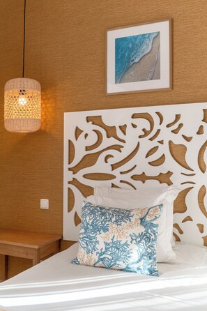 Un dormitorio con cama blanca, cabecera decorativa, un cuadro enmarcado en la pared y una lámpara colgante.