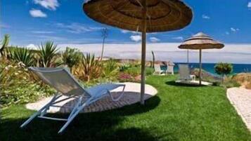 A well-maintained outdoor area with a lawn, two lounge chairs, and two large umbrellas providing shade.