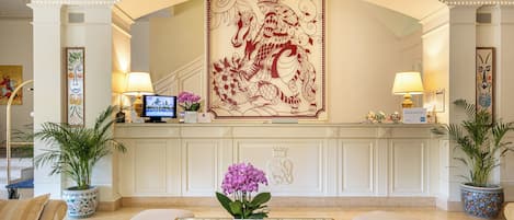 A reception area with a large decorative wall, potted plants, a reception desk, and seating.