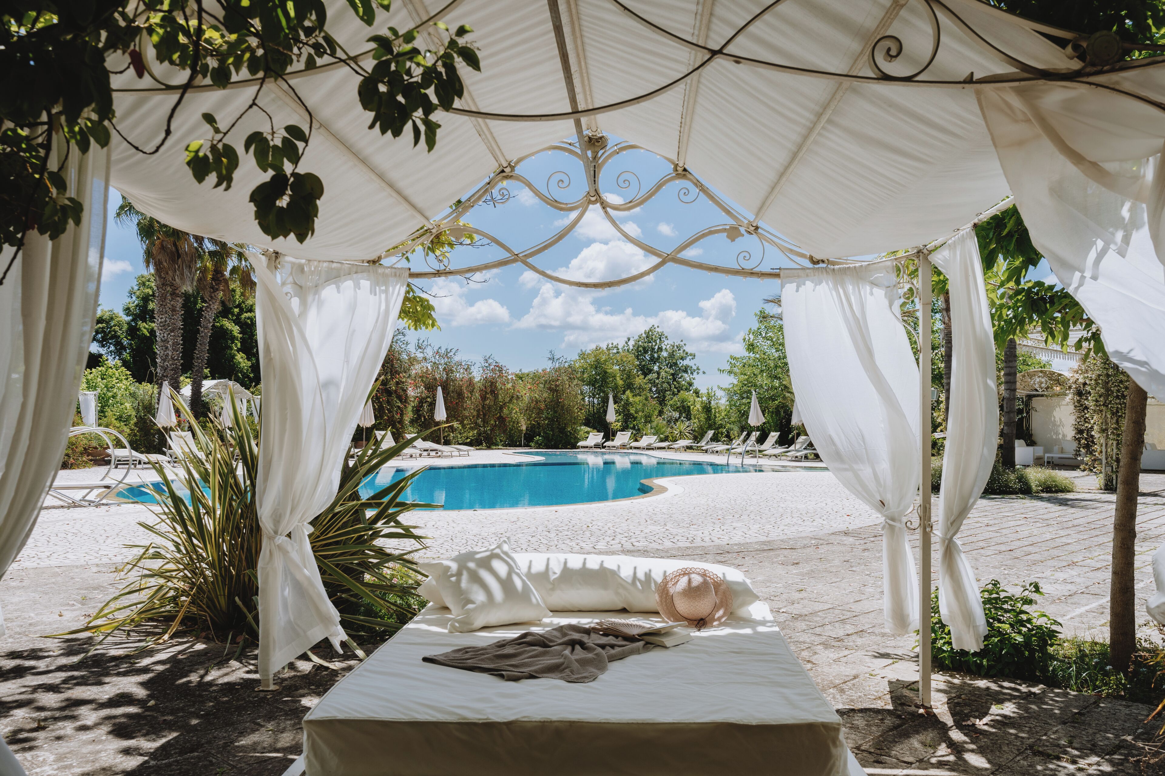 Una cama con dosel, una piscina y sillones de descanso al fondo.