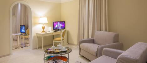 Habitación de hotel con zona de estar, escritorio con computadora, televisor y una mesita con revistas.