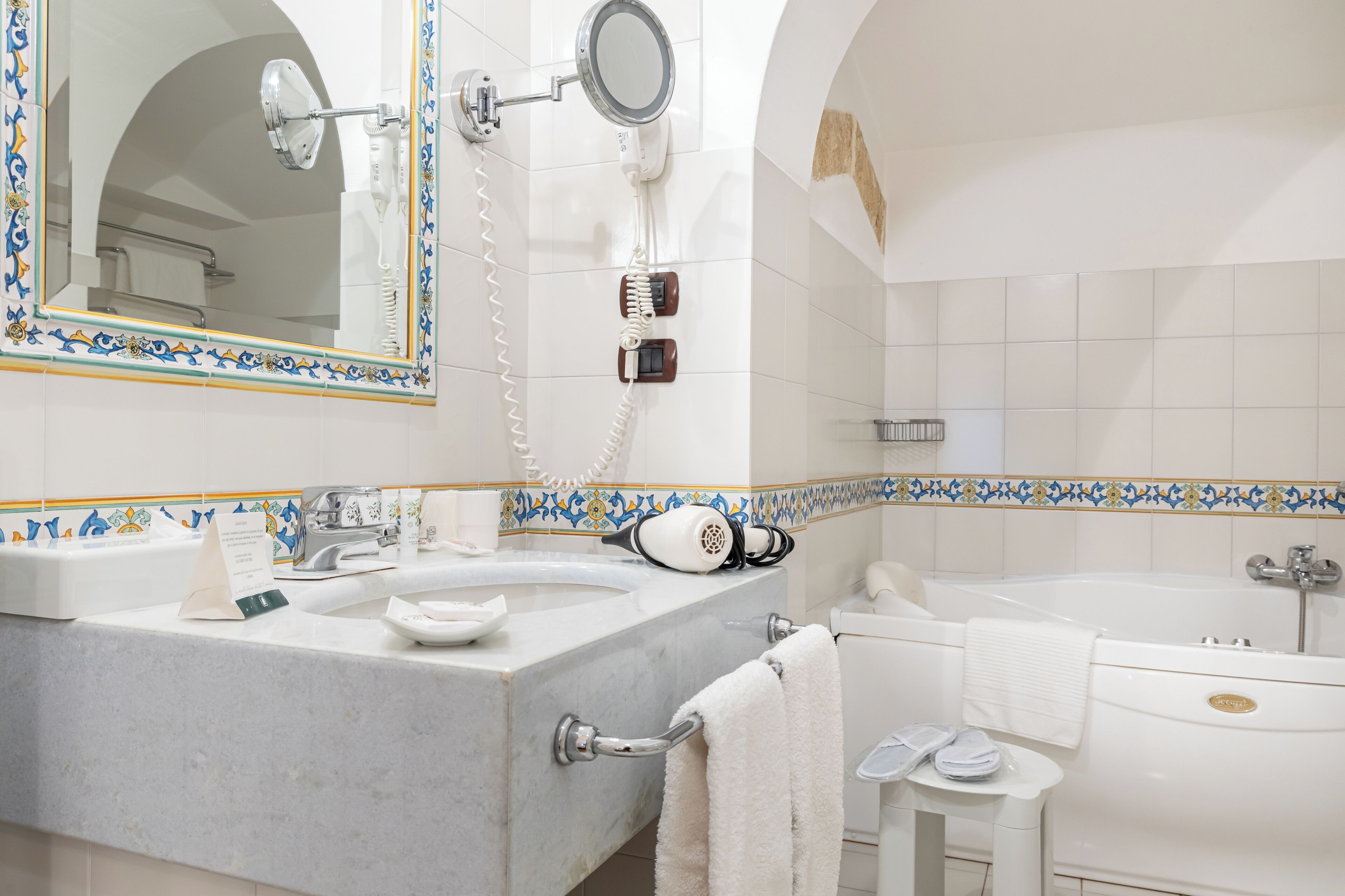 A bathroom with a double sink, a mirror, a hairdryer, a towel rack, and a bathtub.