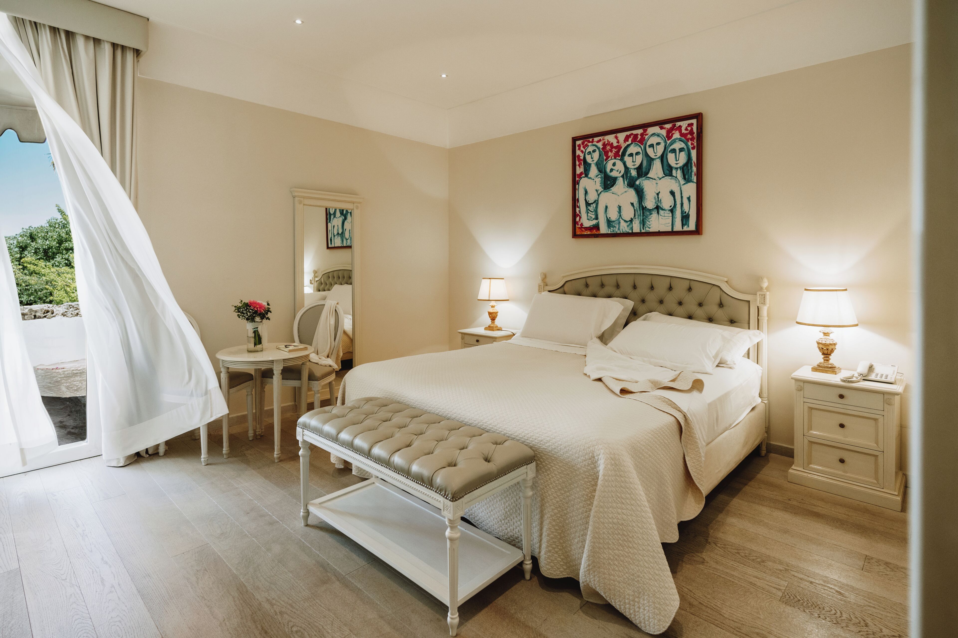 Un dormitorio con cama, mesitas de noche, un banco, un espejo y un cuadro en la pared.