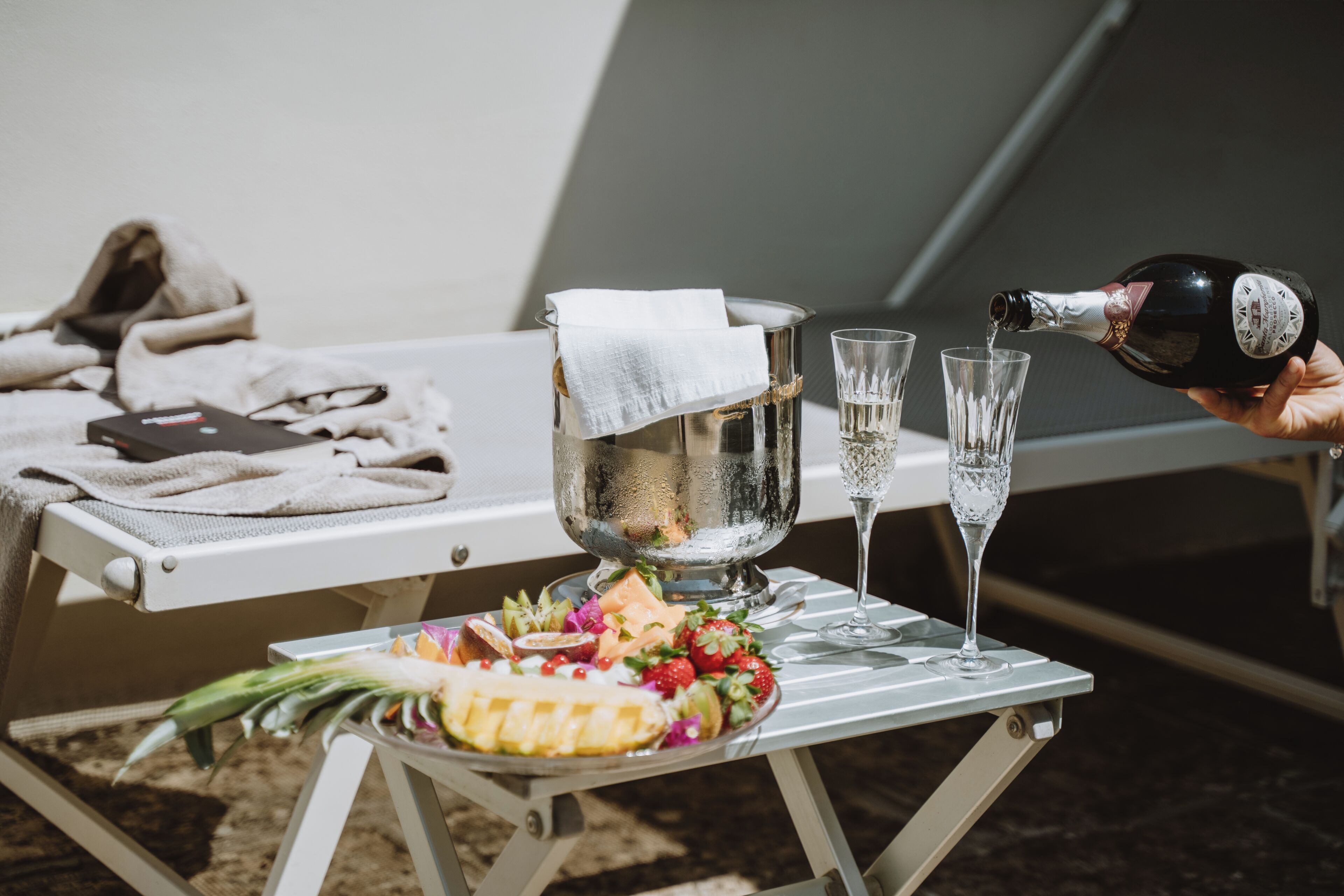 A table with a bottle of champagne, glasses, and a fruit platter.