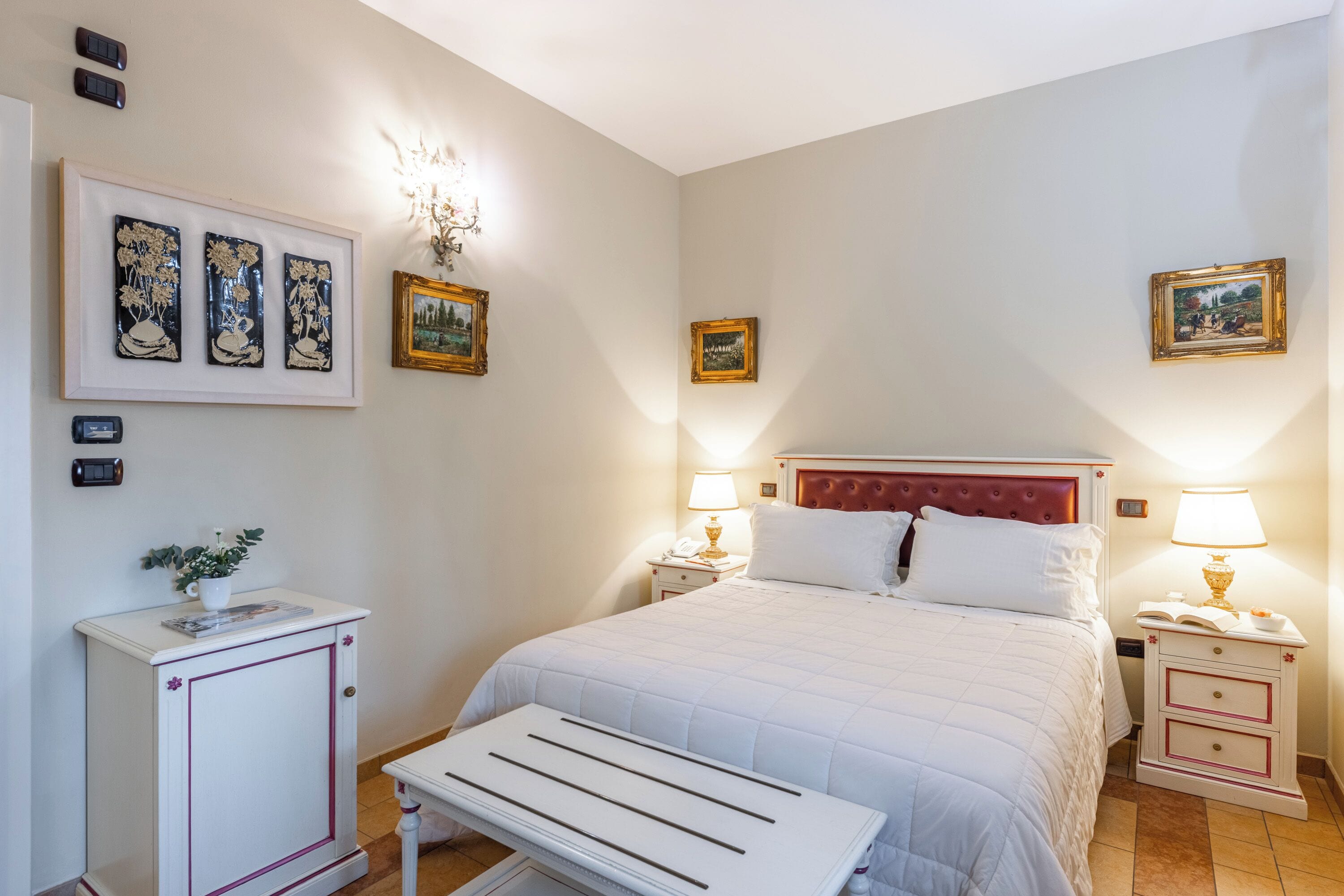 Un dormitorio ordenado con cama, mesitas de noche, un archivador pequeño y obras de arte en la pared.