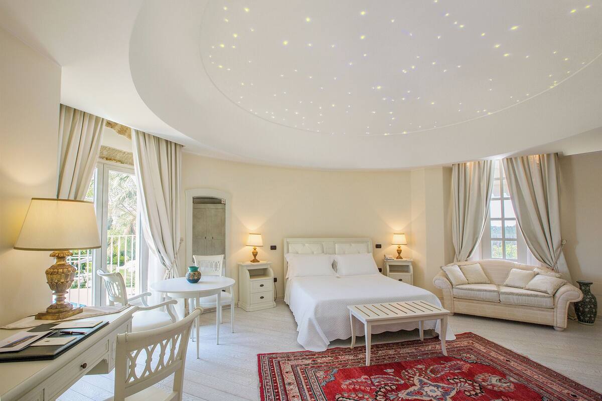 A bedroom with a bed, a desk, a chair, a sofa, and a red patterned rug.