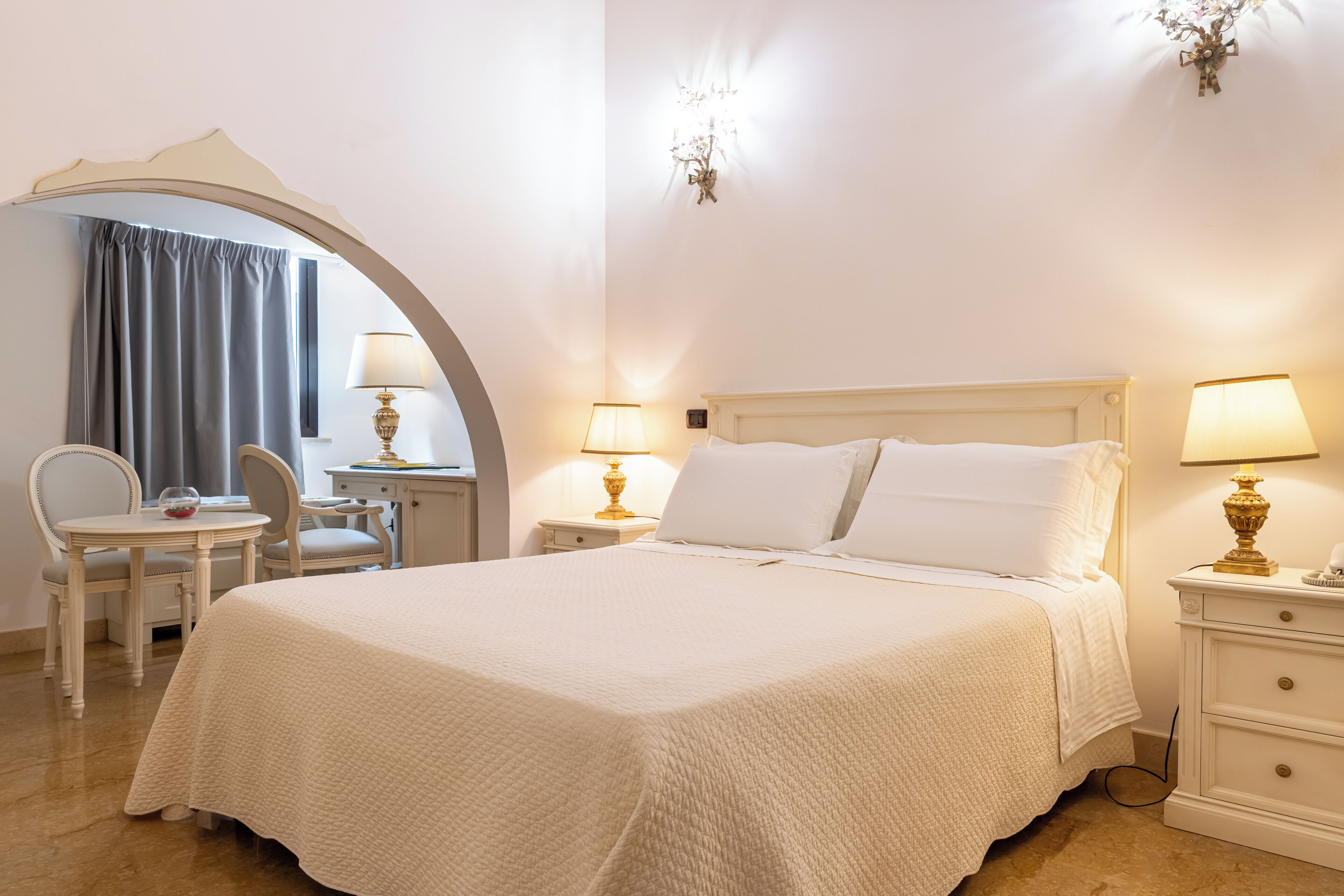 A hotel room with a bed, two bedside tables with lamps, a chair, a desk, and a mirror.