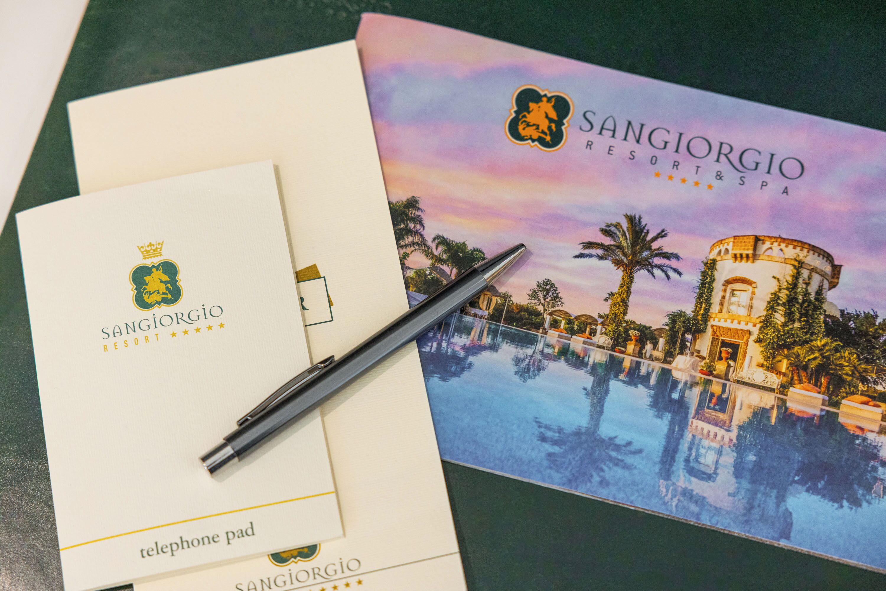 Un folleto del Sangiorgio Resort & Spa que muestra una vista de la piscina, un panel para el teléfono y un bolígrafo.