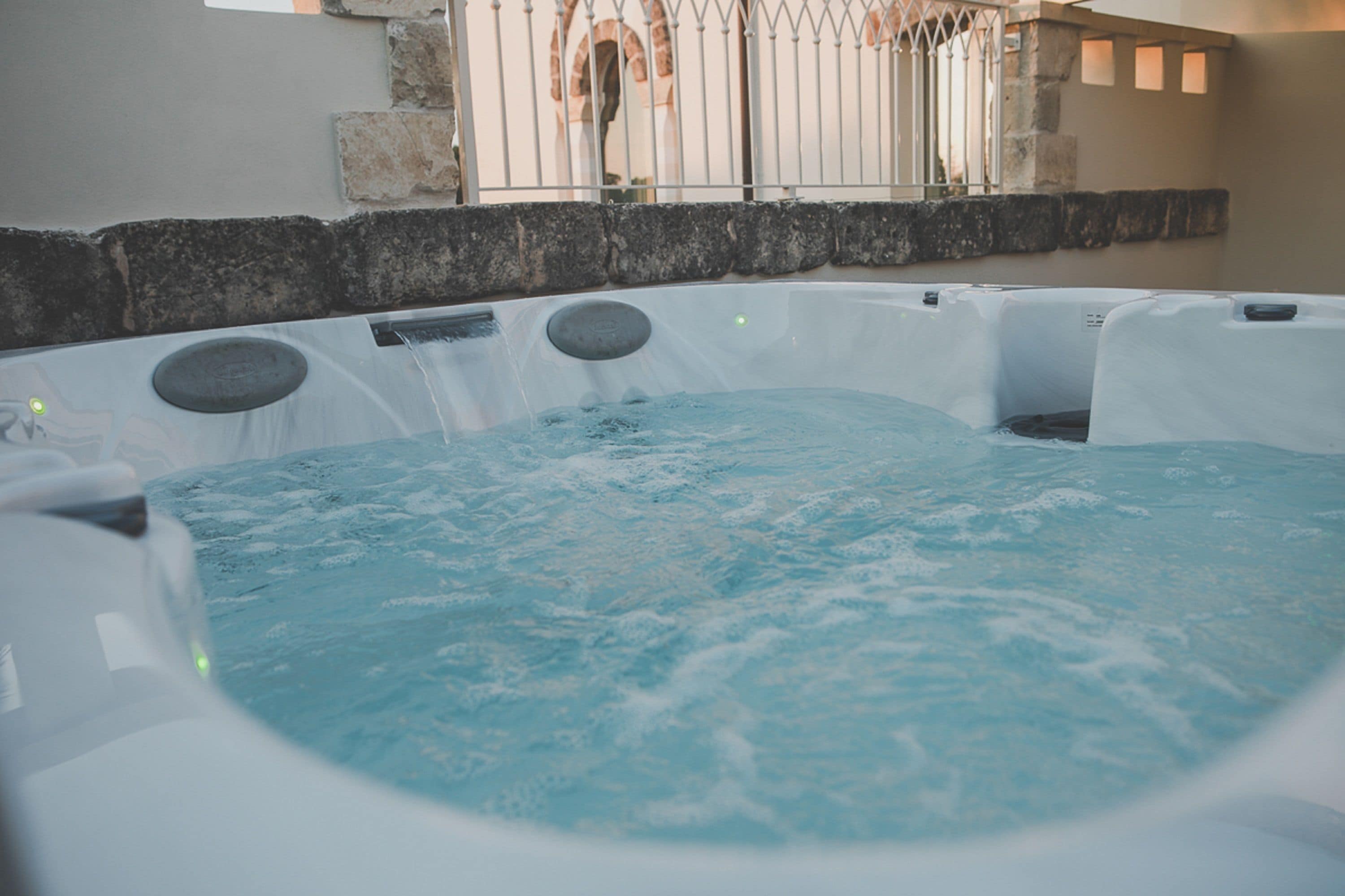 A hot tub with water jets, surrounded by stone walls and a metal fence.