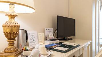 Escritorio de habitación de hotel con una lámpara, un monitor de computadora, una taza de café, un plato con una servilleta y algunos documentos.