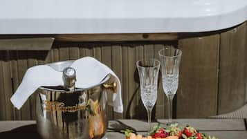 A hot tub with a fruit platter and two glasses on a wooden table.