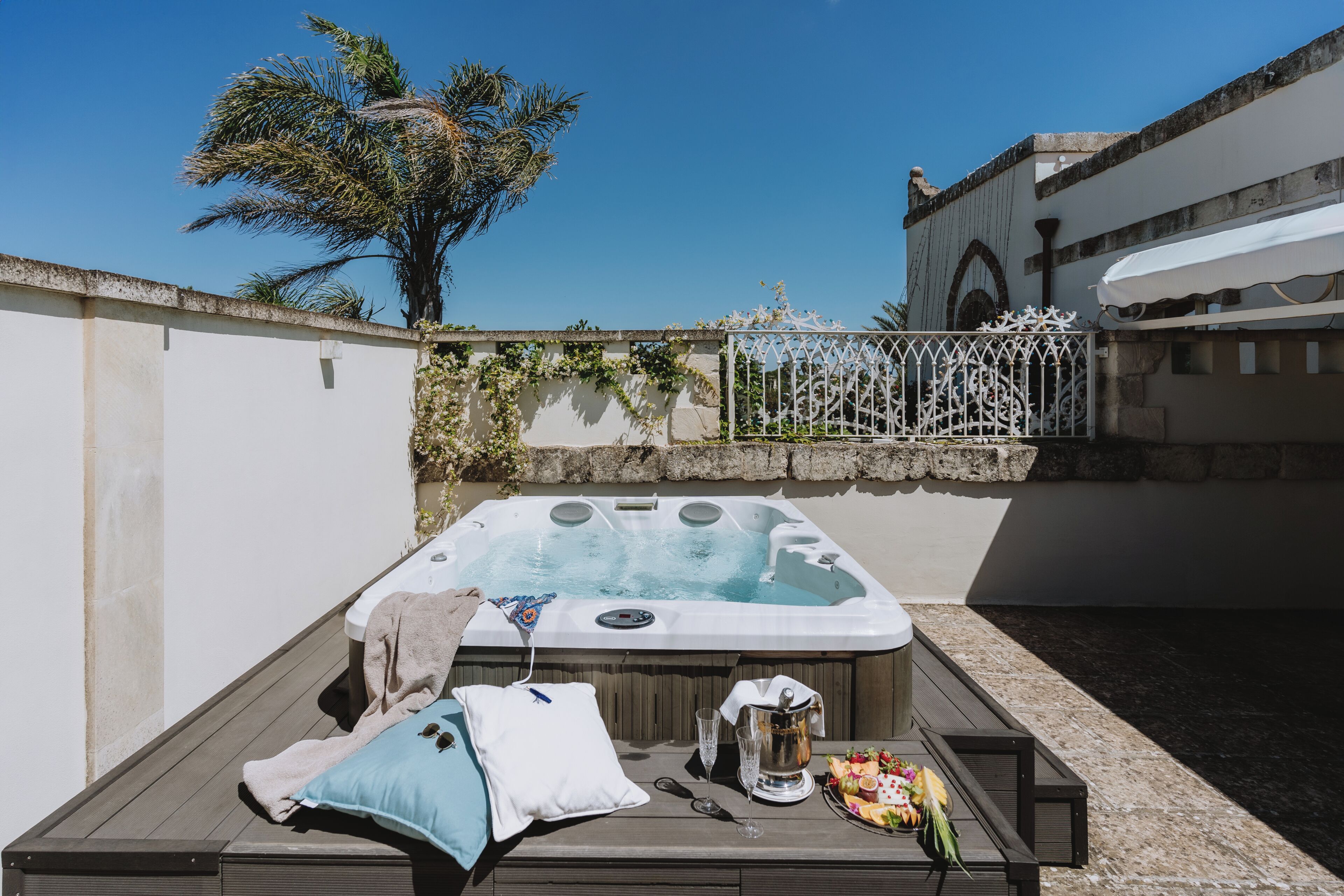 Un bain à remous avec une terrasse en bois, un parasol blanc et une clôture décorative.