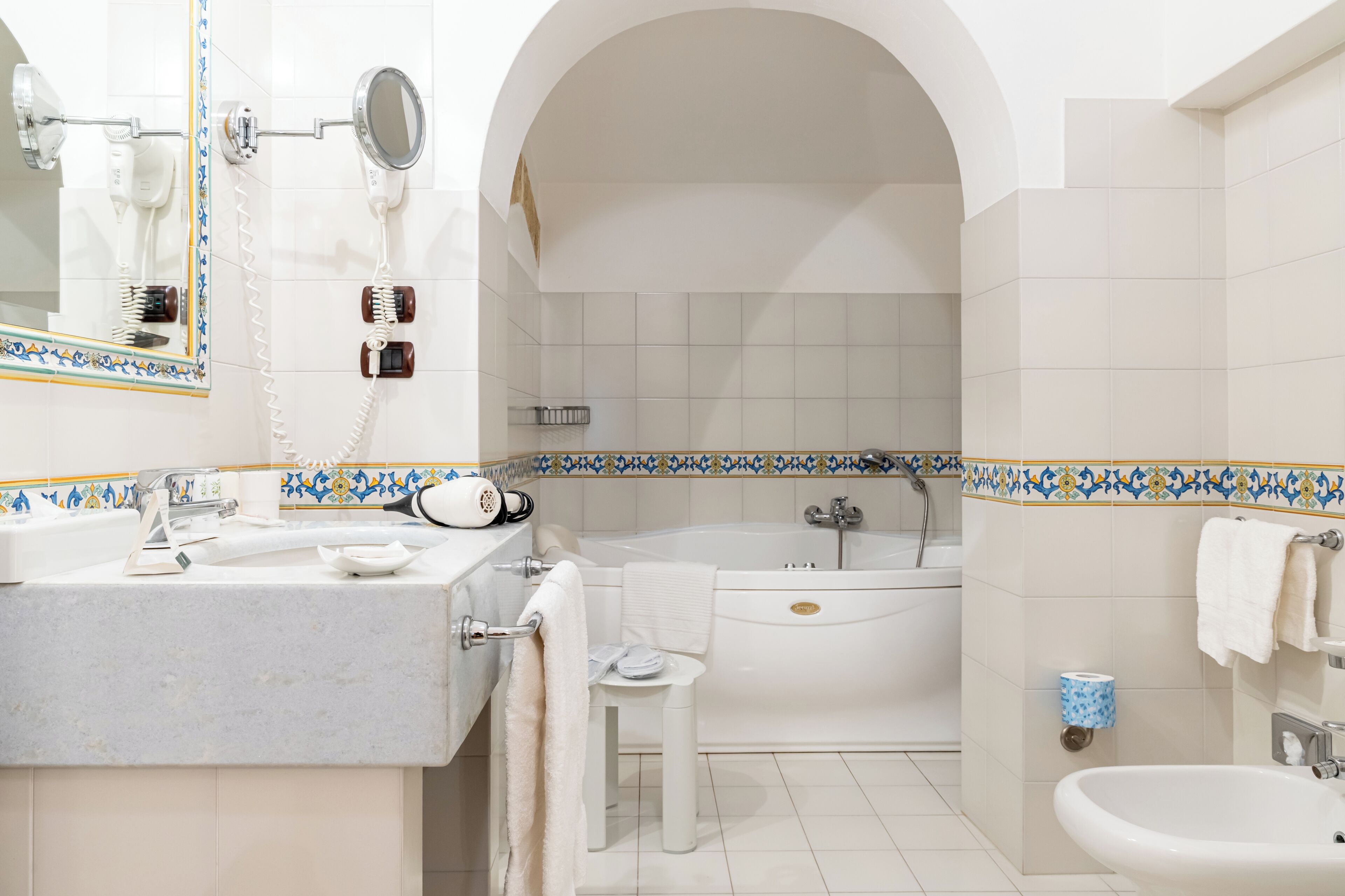 A bathroom with a sink, mirror, hairdryer, and bathtub.
