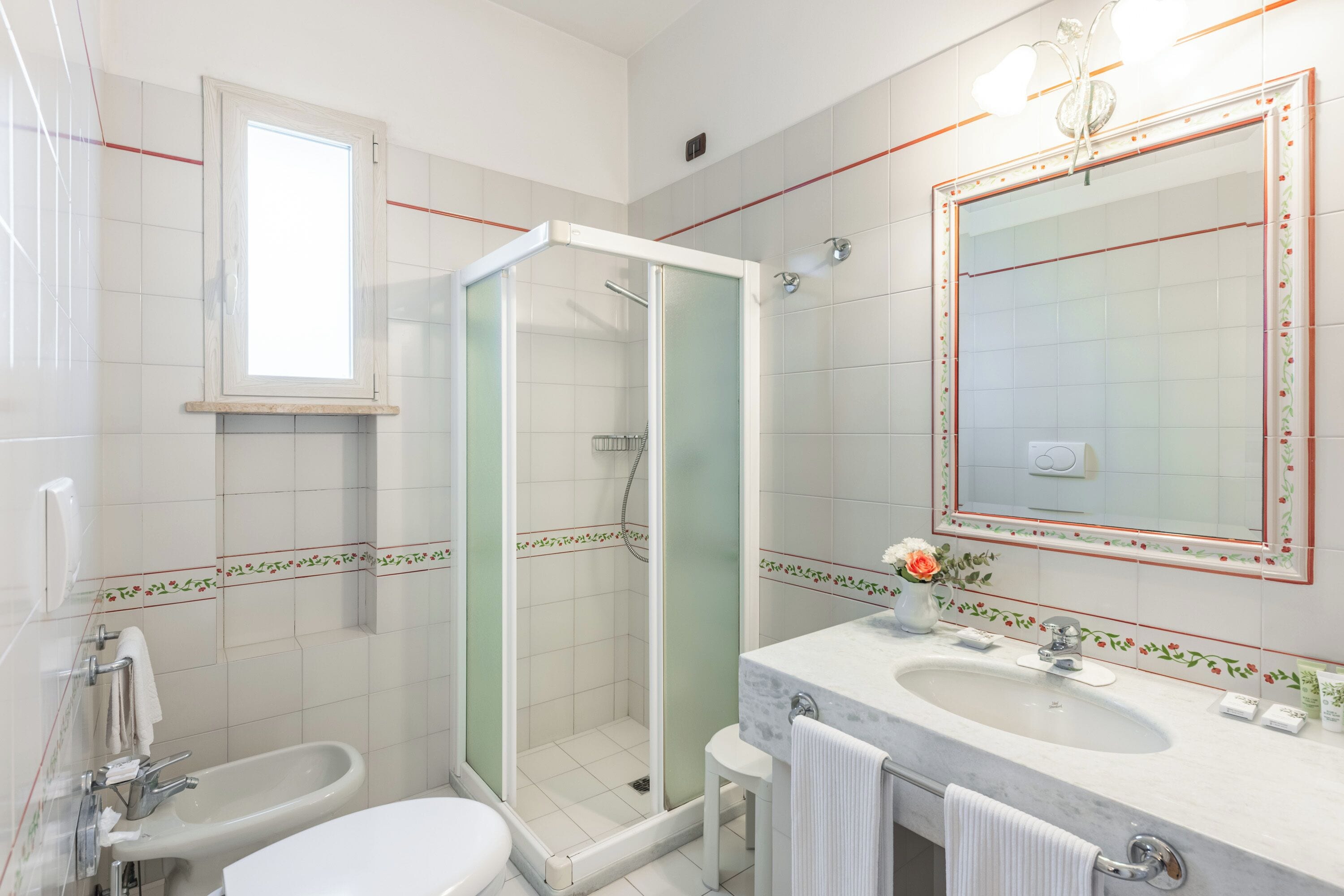 A bathroom with a shower, bidet, sink, and a large mirror with a decorative frame.