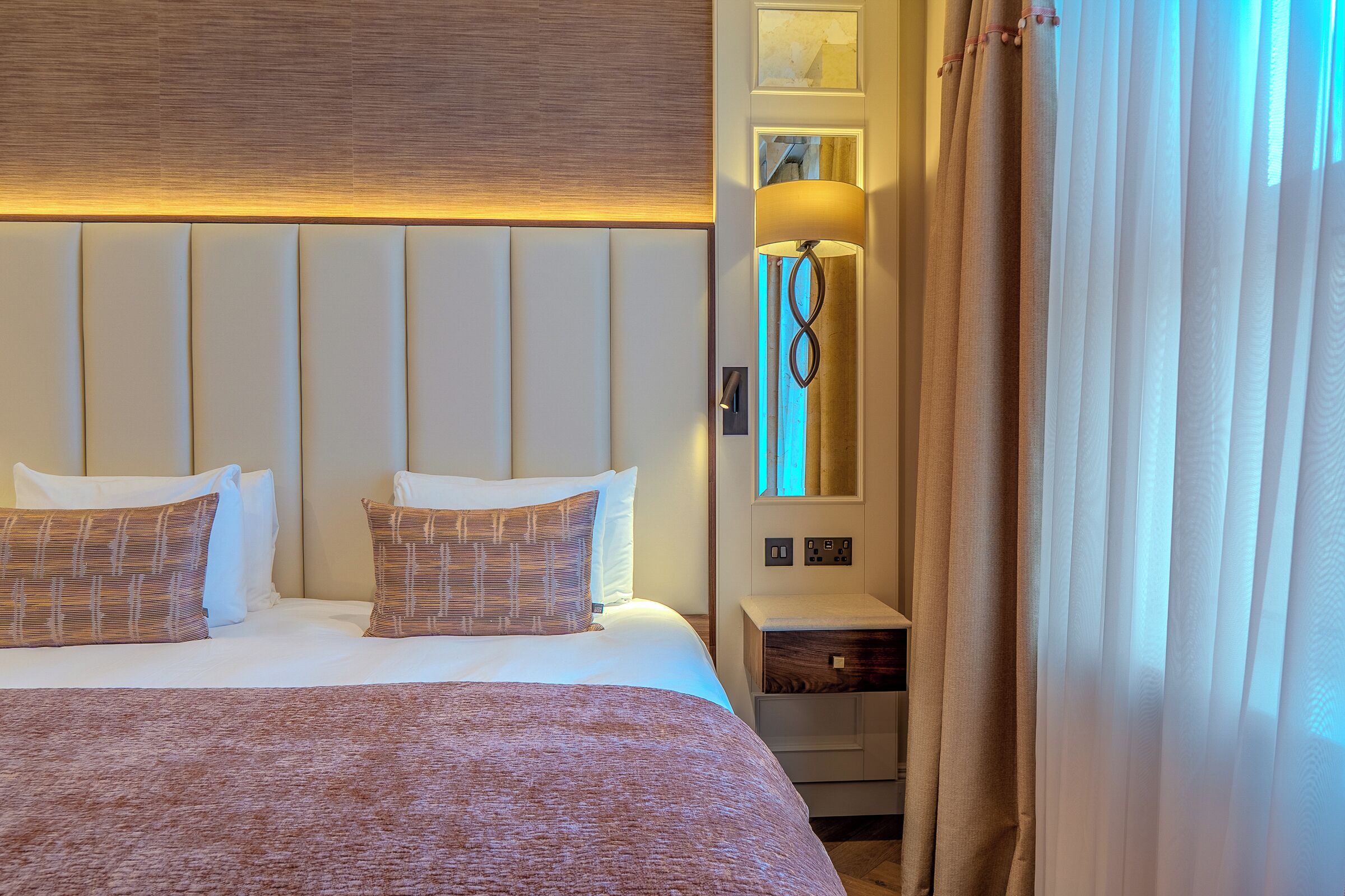 A hotel room with a large bed, a bedside lamp, a nightstand, and a window with curtains.