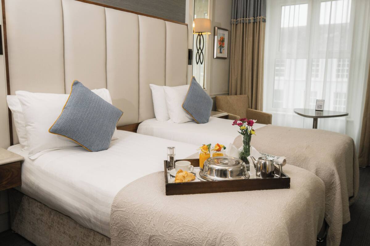 A hotel room with two beds, a small table with breakfast items, and a view of the city through large windows.