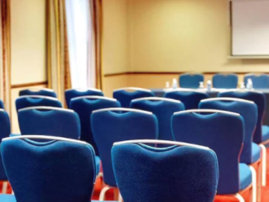 A conference room with rows of blue chairs, a whiteboard, and a projector screen.