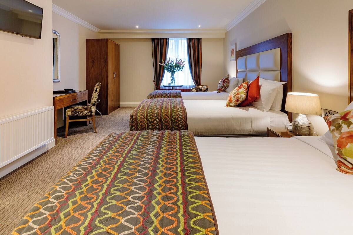 A hotel room with two beds, a desk, a chair, a TV, and a window with curtains.