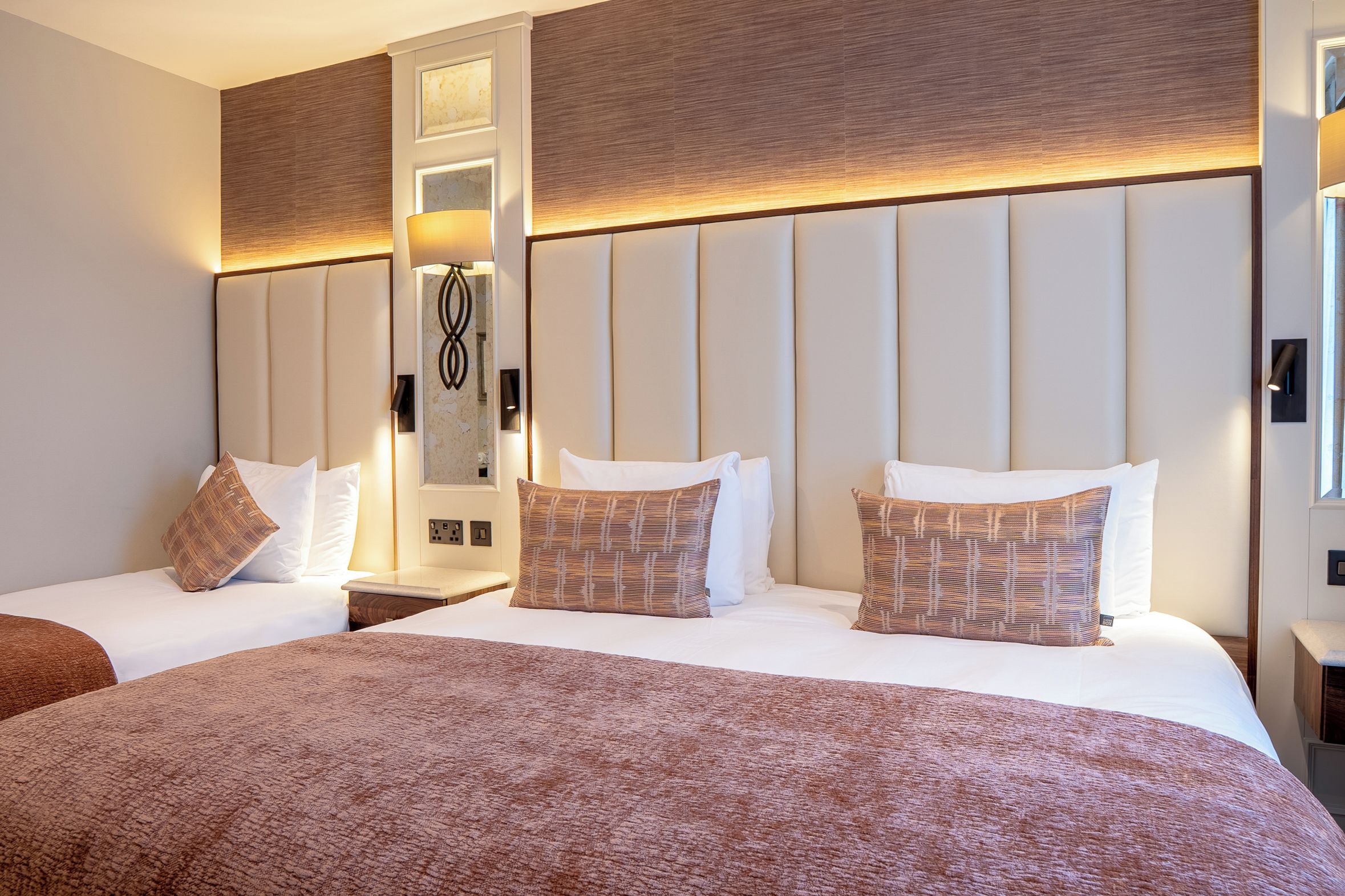A hotel room with a large bed, two bedside tables, a nightstand, a wall-mounted lamp, and a mirror.