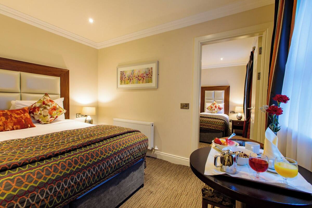 A hotel room with a large bed, a bedside table with a tray of breakfast, a mirror, and a painting on the wall.